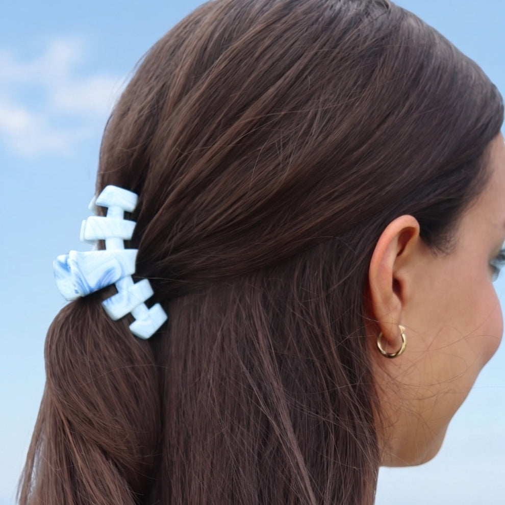 TELETIES blue marbled small claw clip with interlocking teeth, holding back brown hair.
