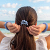 TELETIES blue spiral hair ties, one in ponytail, one on wrist, on a beach.
