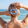 TELETIES blue marbled large flat round hair clip holding blonde hair in a bun at the beach.
