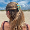 TELETIES By the Sea Shore Small Claw Clip in swirled green and yellow, holding back blonde hair on a beach.
