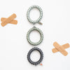 TELETIES Good Hair Rx large spiral hair ties in grey and charcoal with decorative medical-themed charms
