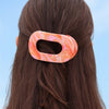 TELETIES Just Keep Swimming Bundle hair clip with pink and orange marble pattern on brown hair against blue sky.
