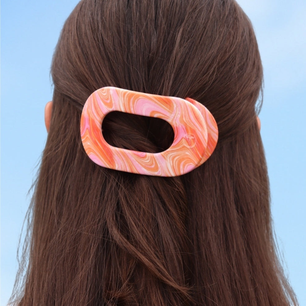 TELETIES Just Keep Swimming Bundle hair clip with pink and orange marble pattern on brown hair against blue sky.
