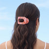 TELETIES Just Keep Swimming small flat round hair clip in pink and orange marbled acetate. Holds back wavy brown hair.
