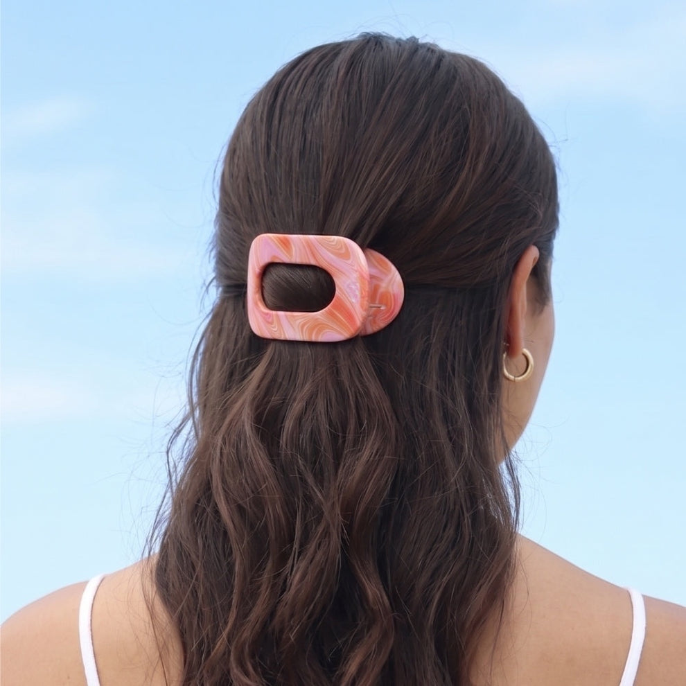 TELETIES Just Keep Swimming small flat round hair clip in pink and orange marbled acetate. Holds back wavy brown hair.
