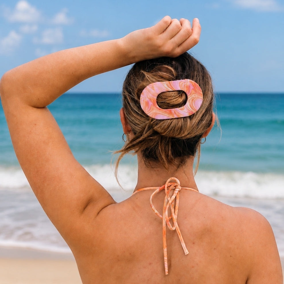 TELETIES Just Keep Swimming large flat oval hair clip in pink and orange marble pattern, holding back blonde hair in a bun.
