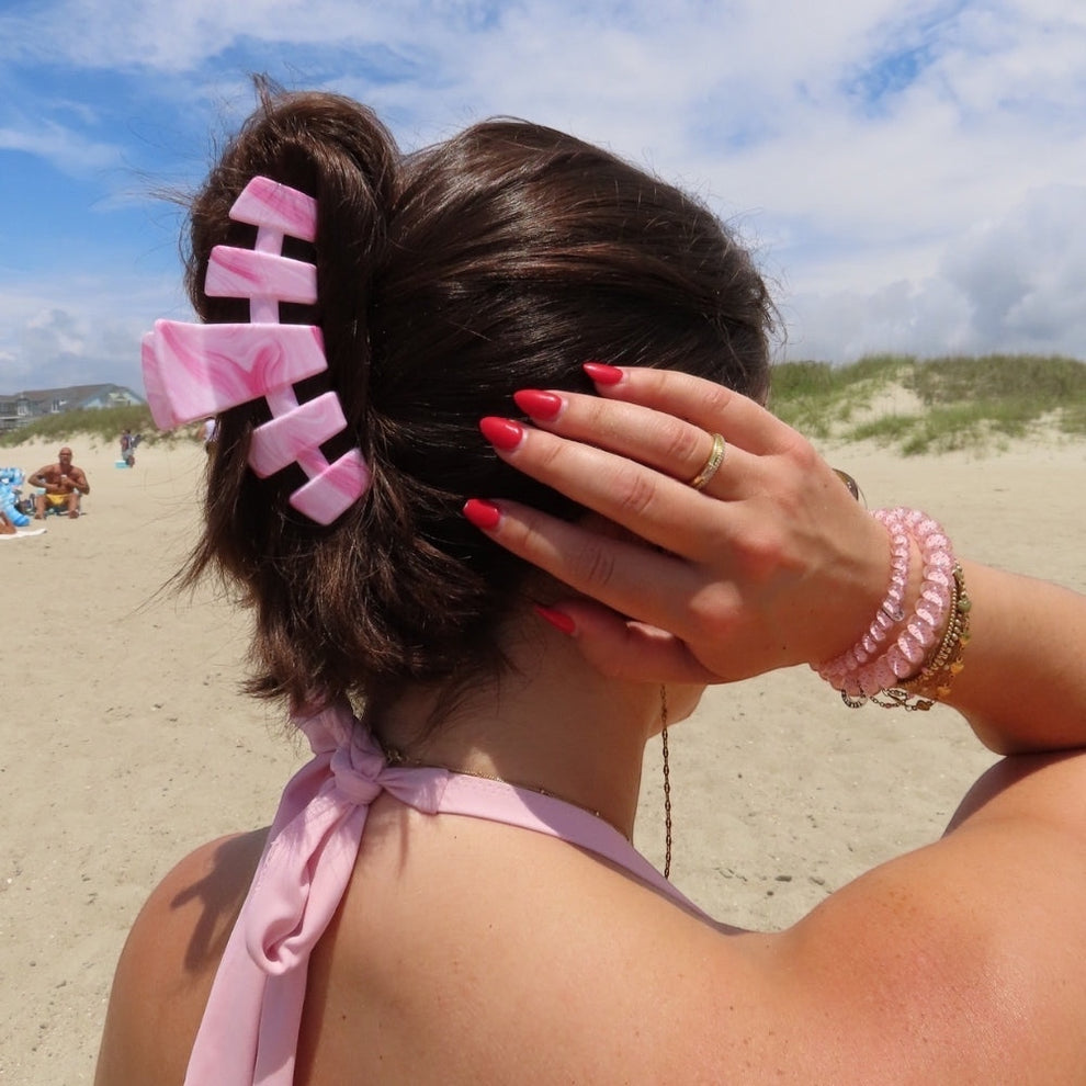 TELETIES Classic Pinch Me! Large pink marble claw clip holding back dark hair on a beach.
