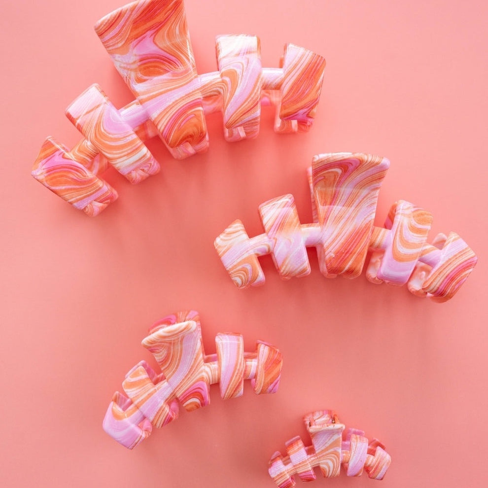 TELETIES medium claw clip in pink and orange marbled swirl pattern. Designed for secure, all-day wear.
