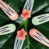 TELETIES Moana snap hair clips featuring floral patterns and pink flower charms on a green leaf background.
