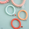 TELETIES Moana mixed pack hair ties in coral, peach, and mint spiral designs with themed charms on a blue background.
