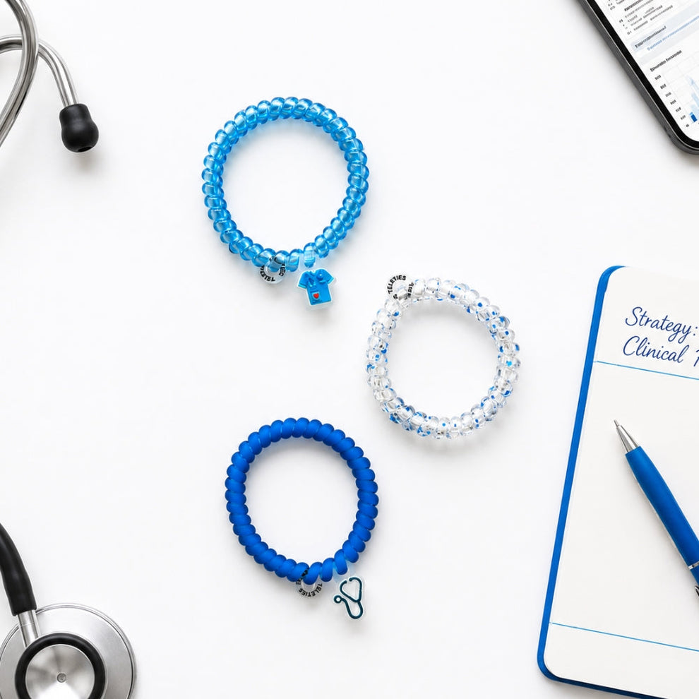 TELETIES On Call small spiral hair ties in blue and clear with medical-themed charms on a desk with a stethoscope.
