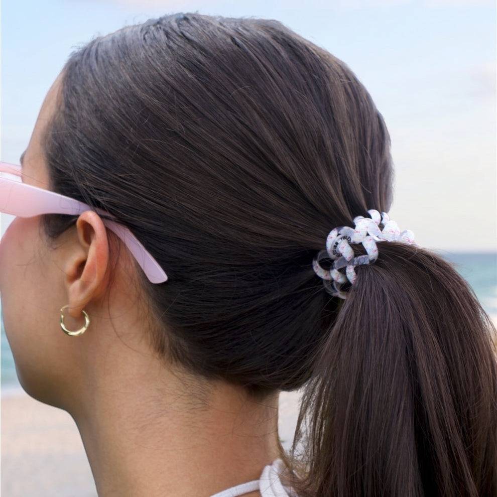 TELETIES Pinch Me! Bundle hair ties in white with pink and grey pattern, holding a ponytail on a woman at the beach.

