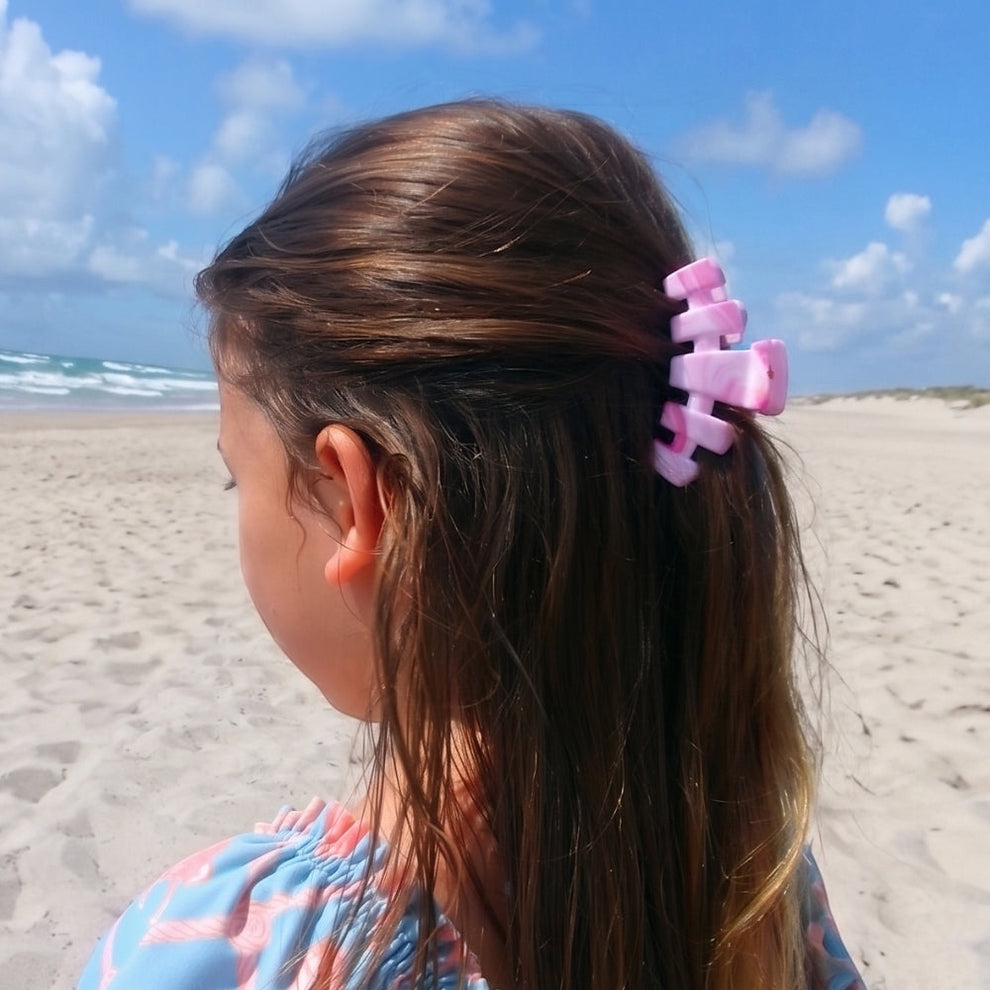 TELETIES Classic Pinch Me! Small pink marbled claw clip holding back brown hair on a beach.
