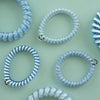 TELETIES small blue spiral hair ties, some with white stripes, others with a blue pattern, sold in packs of three.
