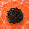 TELETIES black spider web flat hair clip with durable bendable teeth on an orange background
